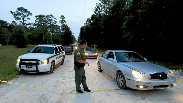 An officer lowers police tape to let cars through at the scene of the shooting in Bell, Florida. Photo: Matt Stamey